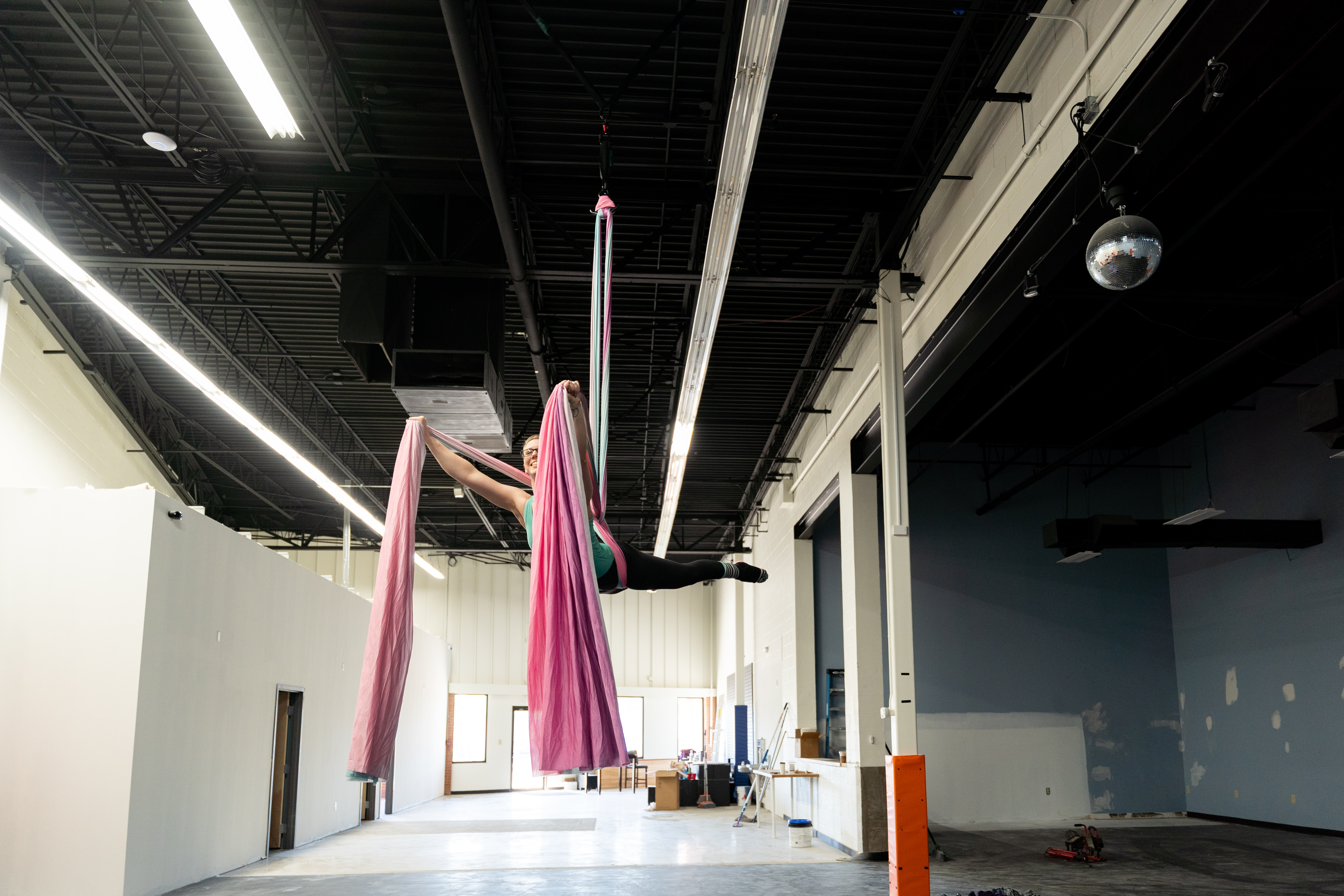 Wide view of the Physio Flows aerial studio showing Aerial Ellen, an aerial instructor, on silks above a safety mat.